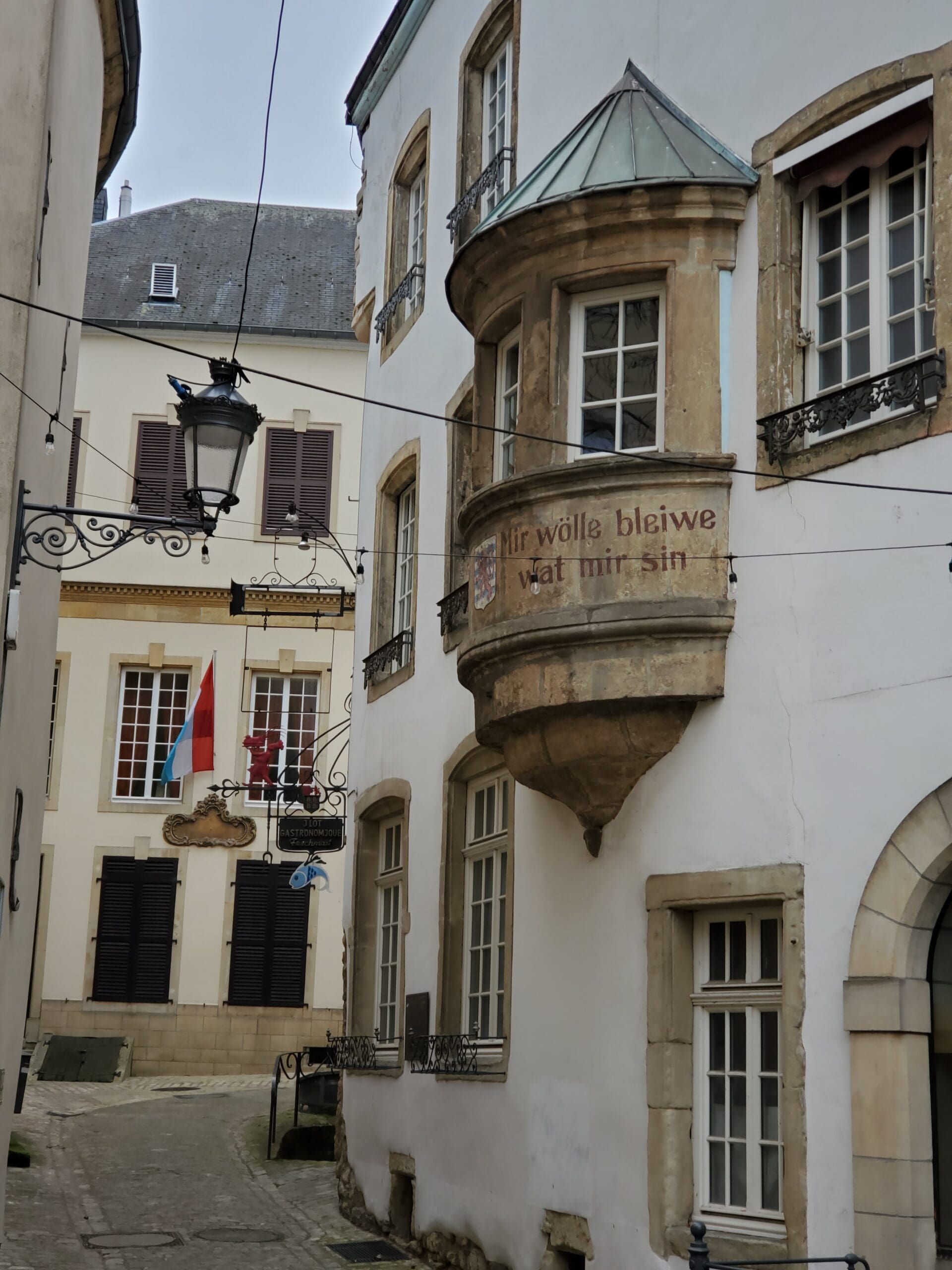 The Luxembourg National motto on the side of the building "Mir wolle bleiwe wat mir sin" which means we want to remain what we are. The Luxembourg flag is in the background.