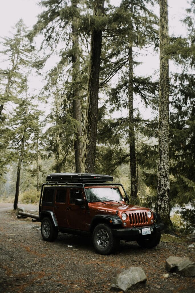 A closed regular full-sized iKamper on a burnt orange four door jeep rubicon wrangler at a gravel parking spot in a forest of douglas fir trees