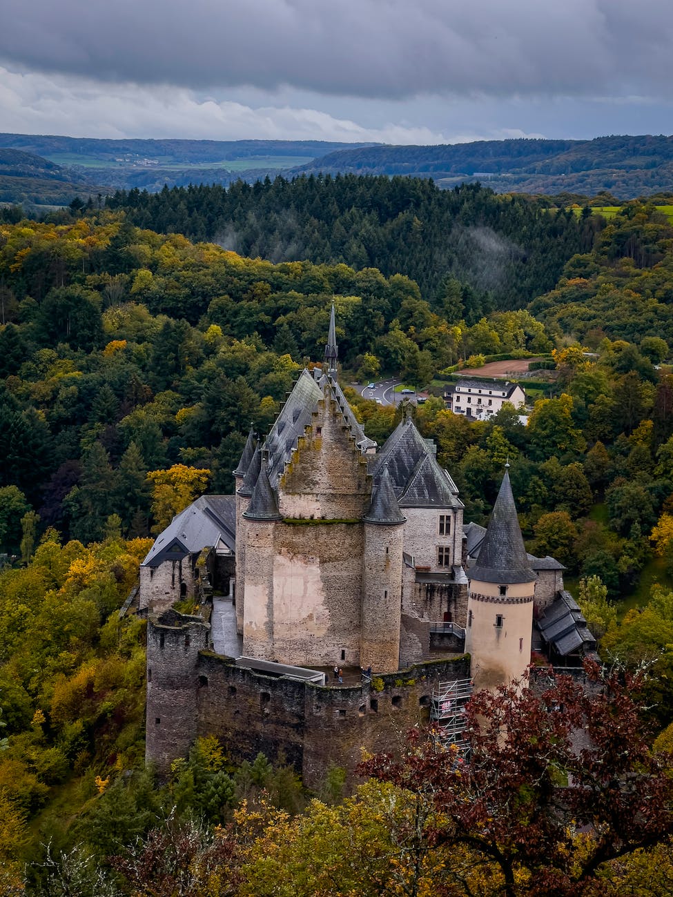 Vianden Castle in Luxembourg, a towering and ancient stone castle on top of a hill surrounded by rolling green hills.