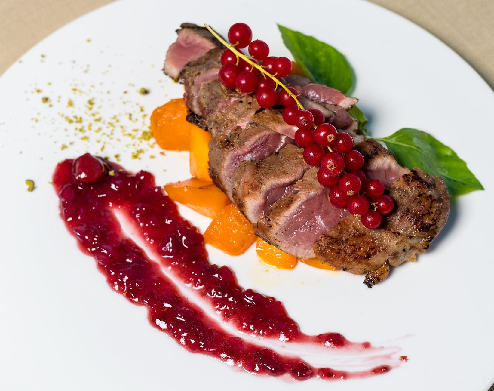 Grilled meat topped with currants and a side of lingoberry sauce on a white plate, displaying modern trends in Icelandic food.