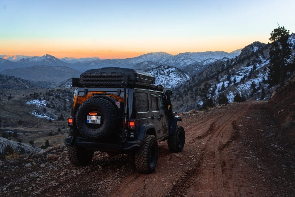 A closed iKamper Rooftop Tent on top of a black jeep wrangler on a dirt mountain high in the rocky mountains with a view of snowcapped peaks