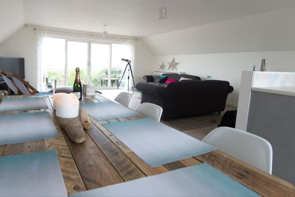 The interior of the beachfront property in Kent featuring a telescope to look at the beach, black couches, and a wooden table
