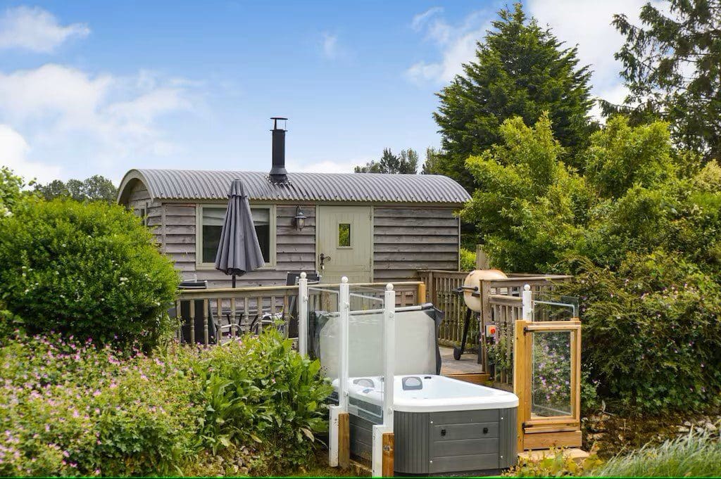 A tiny home cottage with a deck, a hot tub, and a charcoal grill.