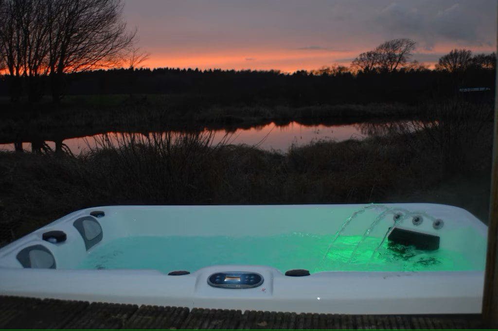 A glowing green hot tub overlooking a lake at sunset.