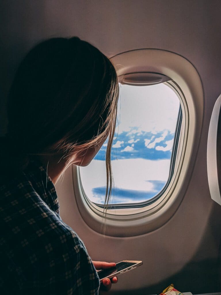 Woman on airplane holding a smartphone. She knows how to watch movies on a plane. Download them before you go!