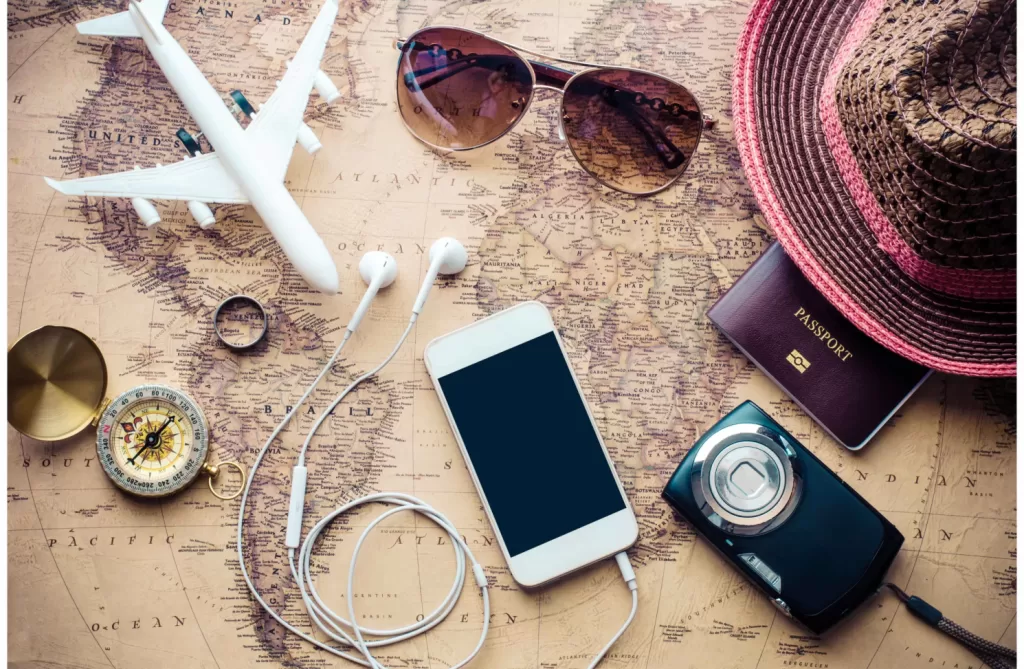 A photo of travel essentials for women including a phone, passport, sunglasses, and a camera on a world map.