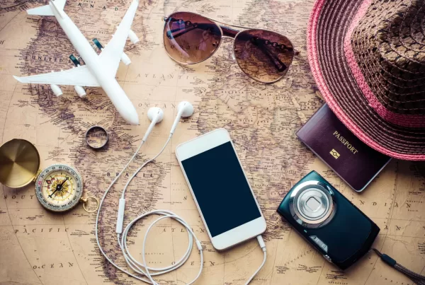 A photo of travel essentials for women including a phone, passport, sunglasses, and a camera on a world map.