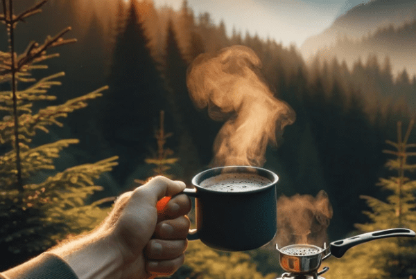 A cup of a man holding instant coffee for backpacking with the sun rising a mountains in the distance.